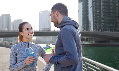 fitness, sport, people and lifestyle concept - smiling couple with bottles of water outdoors over dubai city street background