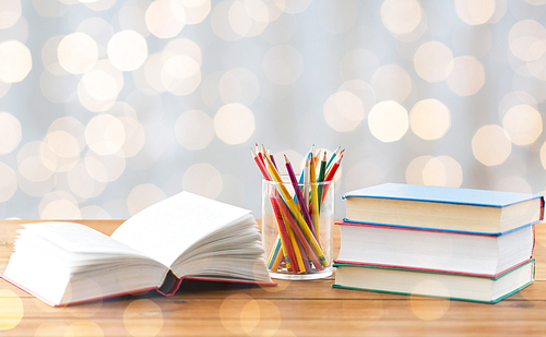 education, school, creativity and object concept - close up of crayons or color pencils and books on wooden table over holidays lights background