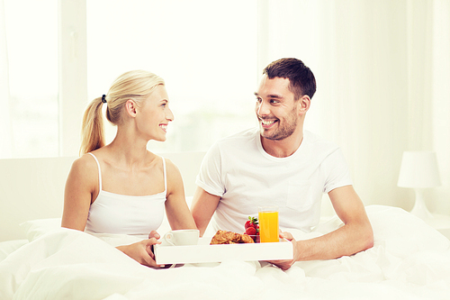 people, love, care and happiness concept - happy couple having breakfast in bed at home