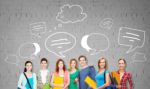 education, school and people concept - group of smiling teenage students with folders and school bags over gray brick wall background with text bubbles