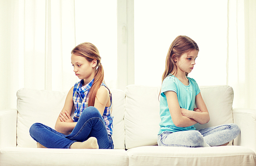 people, children, friends and friendship concept - quarreled angry little girls sitting on sofa back to back at home