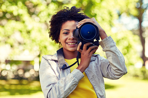 people, photography, technology, leisure and lifestyle - happy young african american female photographer looking to digital camera viewfinder in summer park