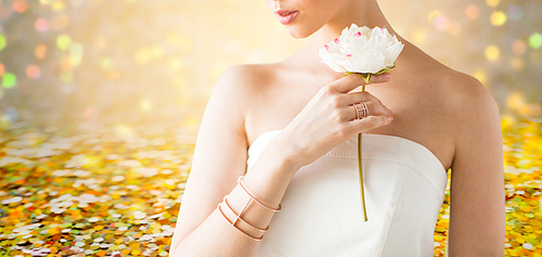 glamour, beauty, jewelry and luxury concept - close up of beautiful woman with golden ring and bracelet holding flower over golden holidays lights background