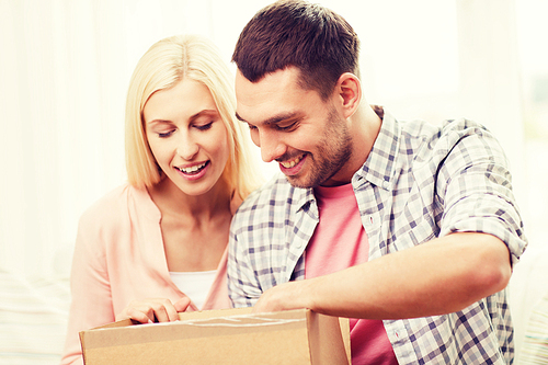 people, delivery, shipping and postal service concept - happy couple opening cardboard box or parcel at home