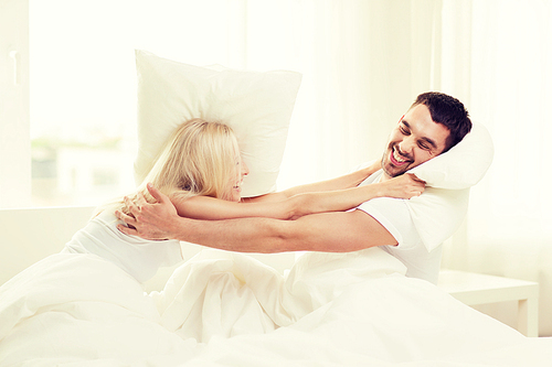 people, family, bedtime and fun concept - happy couple having pillow fight in bed at home