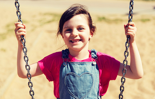 summer, childhood, leisure, friendship and people concept - happy little girl swinging on swing at children playground