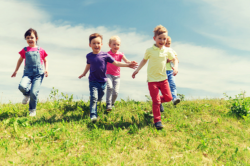 summer, childhood, leisure and people concept - group of happy kids playing tag game and running on green field outdoors