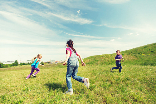 summer, childhood, leisure and people concept - group of happy kids playing tag game and running on green field outdoors