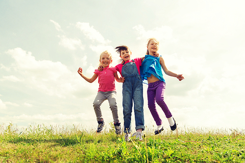 summer, childhood, leisure and people concept - group of happy kids jumping high on green field outdoors