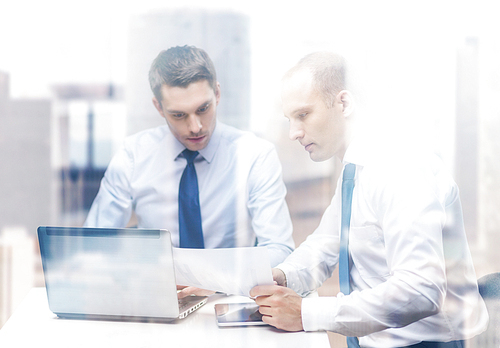 business, technology and office concept - two businessmen with laptop, tablet pc computer and papers having discussion in office