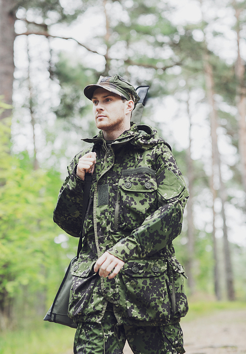 hunting, war, army and people concept - young soldier, ranger or hunter with gun walking in forest