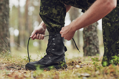 war, hiking, army and people concept - close up of soldier boots and hands tying bootlaces in forest