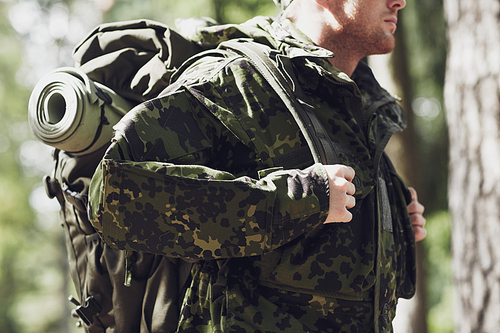 war, hiking, army and people concept - close up of young soldier, ranger or hunter with backpack walking in forest