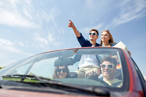 leisure, road trip, travel and people concept - happy friends with map driving in cabriolet car along country road and pointing finger to something ahead