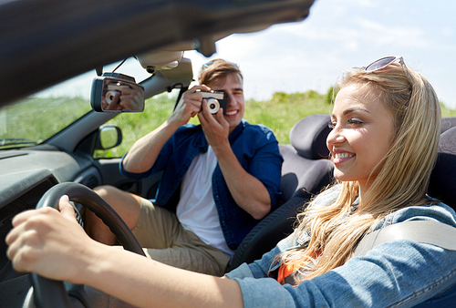 leisure, road trip, travel and people concept - happy couple driving in cabriolet car and taking picture by film camera