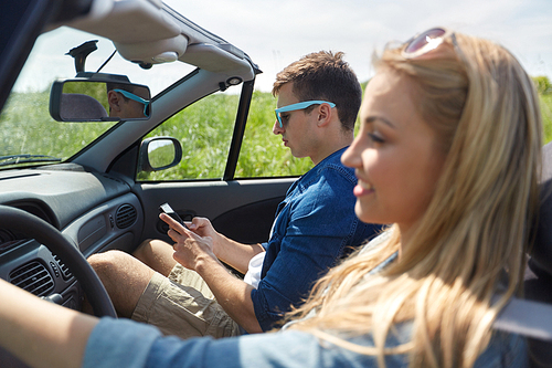 leisure, road trip, travel and people concept - man texting on smartphone driving in cabriolet car with his girlfriend