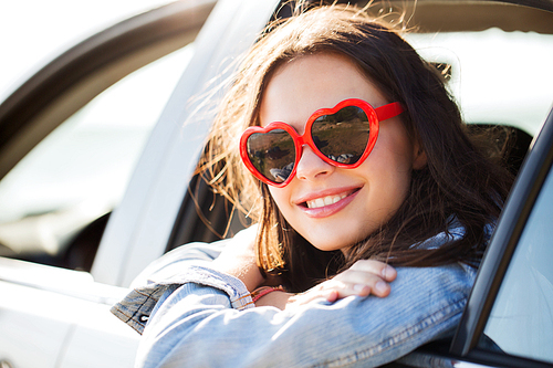 summer holidays, valentines day, travel, road trip and people concept - happy teenage girl or young woman heart shaped sunglasses in car