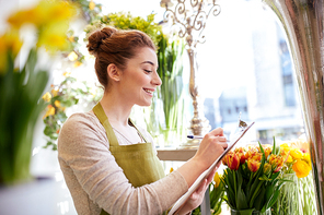 people, sale, retail, business and floristry concept - happy smiling florist woman with clipboard writing and making notes order at flower shop