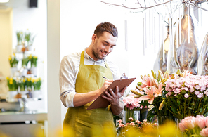 people, sale, retail, business and floristry concept - happy smiling florist man with clipboard writing and making notes order at flower shop