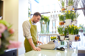 people, sale, retail, business and floristry concept - happy smiling florist man with cashbox standing at flower shop counter