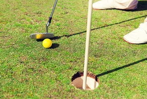 game, entertainment, sport, people and leisure concept - close up of man playing golf and putting ball with metal club into hole on golf field