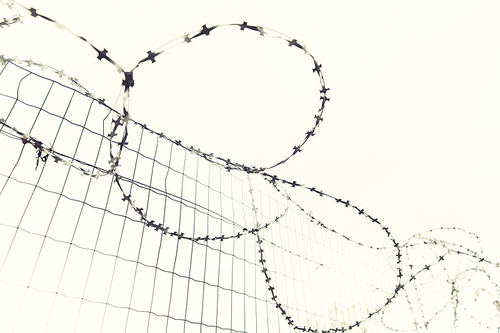 imprisonment, restriction concept - barb wire fence over gray sky