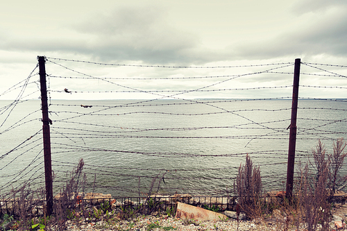 imprisonment, restriction concept - barb wire fence over gray sky and sea