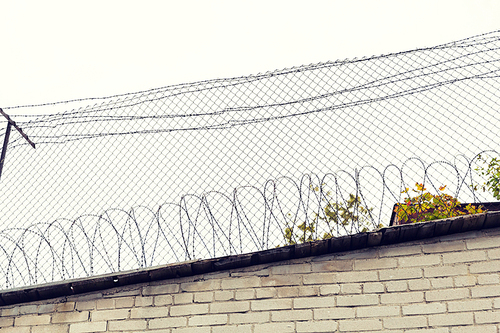 imprisonment, restriction concept - barb wire fence and brick wall over gray sky