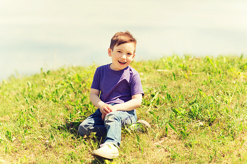 summer, childhood, leisure and people concept - happy little boy sitting on grass outdoors