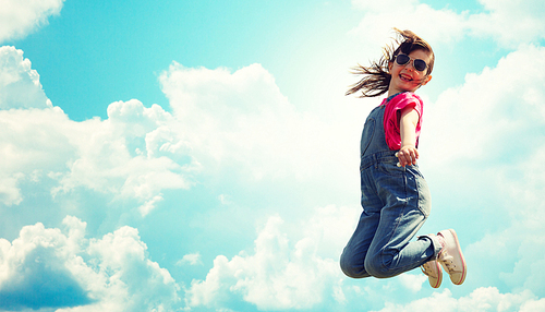 summer, childhood, leisure and people concept - happy little girl jumping high over blue sky and clouds background