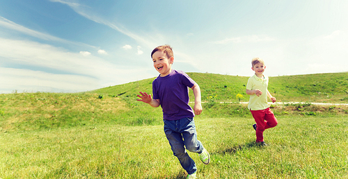 summer, childhood, leisure and people concept - happy little boys playing tag game and running outdoors on green field