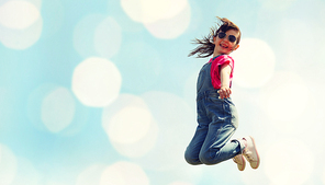 summer, childhood, leisure and people concept - happy little girl jumping high over blue sky and lights background