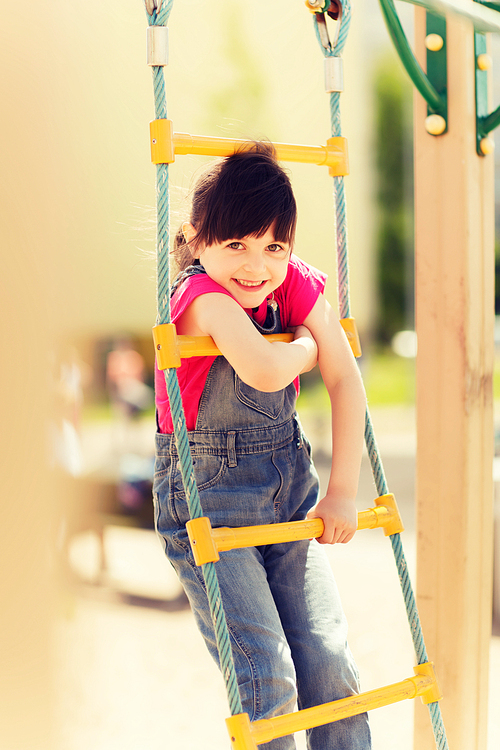 summer, childhood, leisure and people concept - happy little girl on children playground climbing by rope-ladder