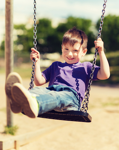 summer, childhood, leisure, friendship and people concept - happy little boy swinging on swing at children playground