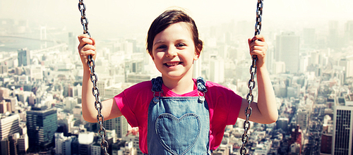 summer, childhood, leisure, friendship and people concept - happy little girl swinging on swing over city background