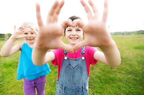 summer, childhood, leisure, gesture and people concept - happy little girls showing heart shape hand sign outdoors