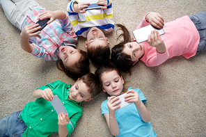 childhood, fashion, friendship and people concept - group of happy smiling little children with smartphones lying on floor