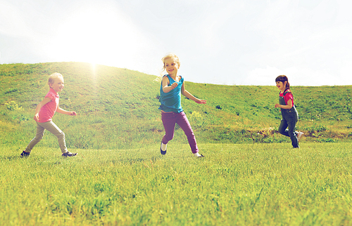 summer, childhood, leisure and people concept - group of happy kids playing tag game and running on green field outdoors