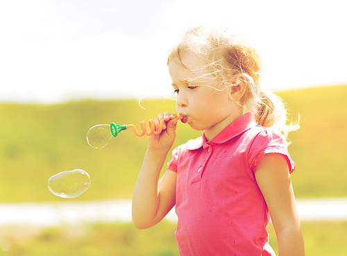 summer, childhood, leisure and people concept - little girl blowing soap bubbles outdoors