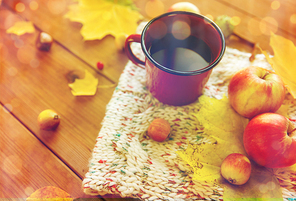 season, drink and morning concept - close up of tea cup on wooden table with autumn leaves and scarf