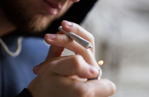 drug use, substance abuse, addiction, people and smoking concept - close up of addict lighting up marijuana joint with lighter