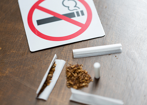 drug use, substance abuse, addiction and no smoking concept - close up of marijuana or handmade cigarette with prohibiting sign