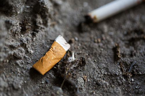 smoking, substance abuse, addiction, people and bad habits concept - close up of smoked cigarette butt on ground