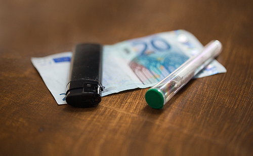 substance abuse, addiction, drug sale and smoking concept - close up of marijuana joint tube, money and lighter on table