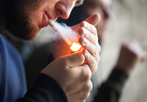 smoking, substance abuse, addiction and bad habits concept - close up of young people lighting cigarette outdoors