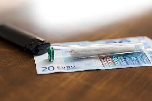 substance abuse, addiction, drug sale and smoking concept - close up of marijuana joint tube, money and lighter on table