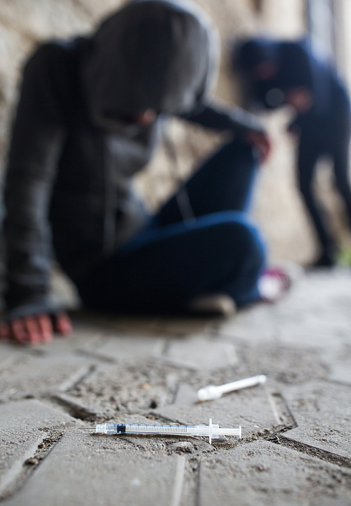 substance abuse, addiction, people and drug use concept - close up of addicts and used syringes on ground