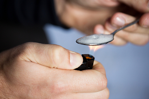 drug use, crime, addiction, substance abuse and people concept - close up of addict with lighter and spoon preparing dose of crack cocaine on street