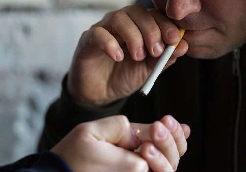 smoking, substance abuse, addiction and bad habits concept - close up of young people lighting cigarette outdoors