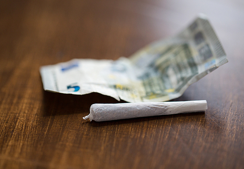 substance abuse, nicotine addiction, drug sale and smoking concept - close up of marijuana joint and money